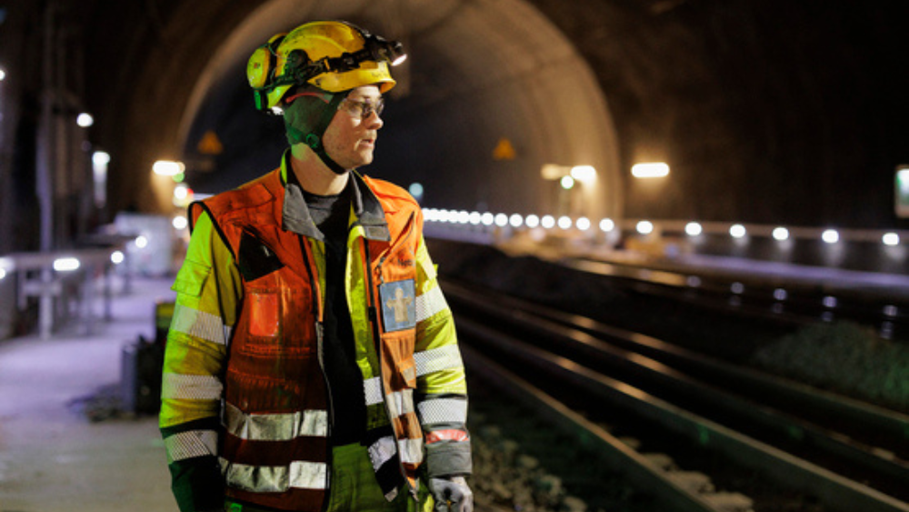 Energimontør i tunnel med gul hjelm og oransje vest ser bort fra kamera.